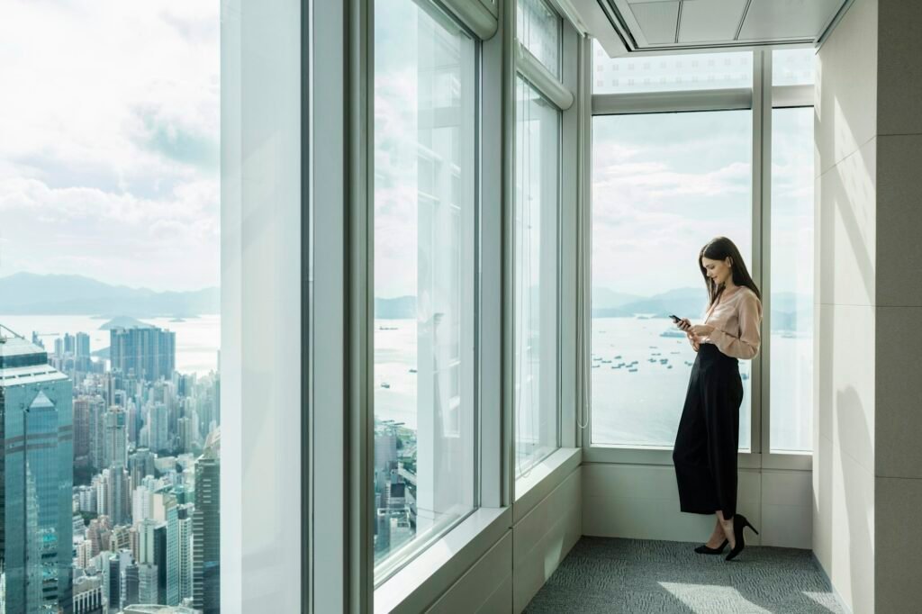 Business woman in skyscraper office window using smartphone